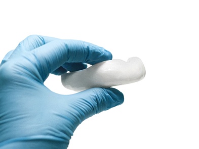 Gloved hand holding durable white athletic mouthguard