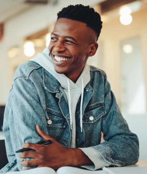 Young man in denim jacket smiling while sitting at desk