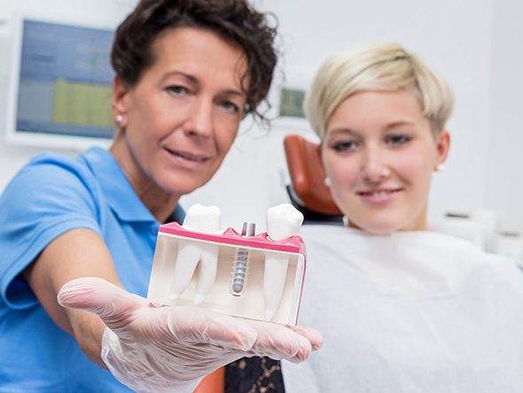 Dentist showing a patient a dental implant model