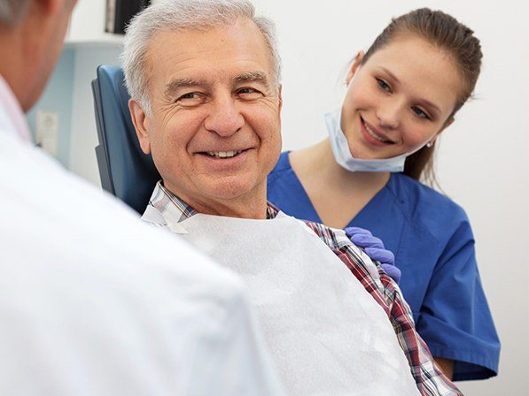 Man discussing paying for dental implant tooth replacement with oral surgery team members