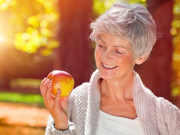 Smiling woman eating an apple after dental implant supported tooth replacement
