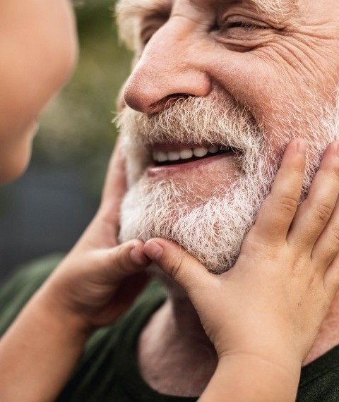 Older man smiling at grandson after receiving full mouth dental implants