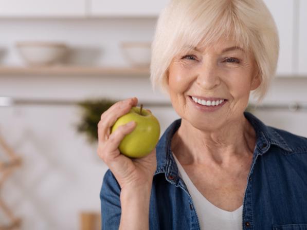 Older woman with full mouth dental implants eating an apple