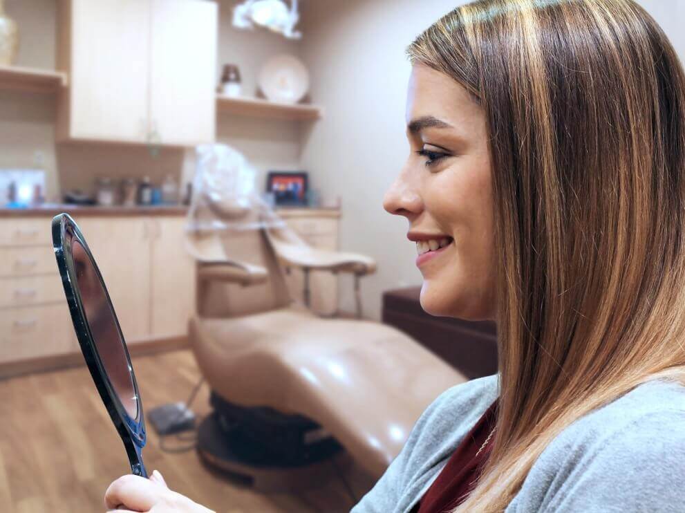Woman looking at her smile in mirror at oral surgery office