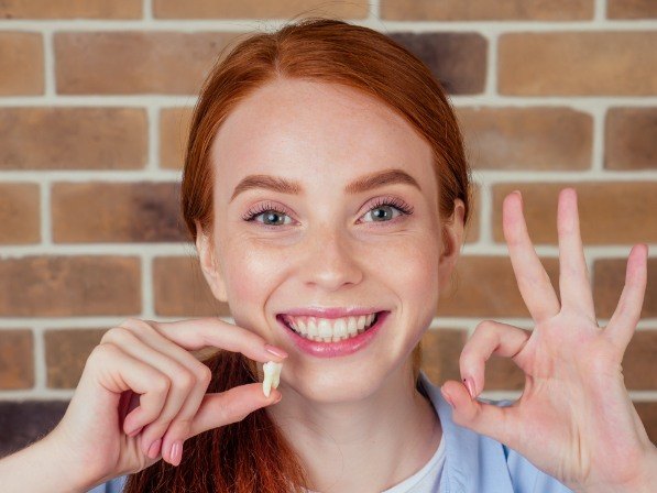 Smiling woman holding wisdom tooth after removal