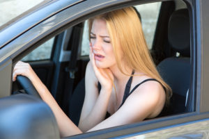 woman with toothache holding cheek while driving